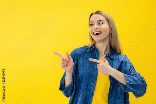 Positive woman smiles positively recommends using blank space indicates at upper left corner dressed in casual wear over vivid yellow background shows direction or way