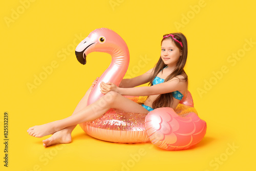 Cute little happy girl in swimsuit with inflatable ring and goggles sitting on yellow background