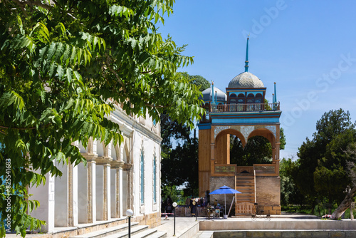 Panoramic view of the Emir's Summer Palace in Bukhara, framed by lush foliage, with a detailed pavilion in the background. Bukhara, Uzbekistan