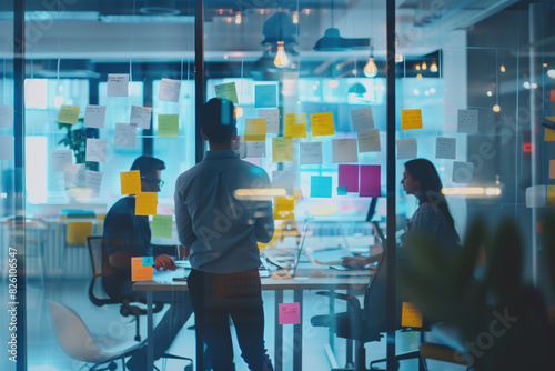 Brainstorming session in a bright contemporary workspace with team members using sticky notes on a glass wall to map out their tech startup's business strategy