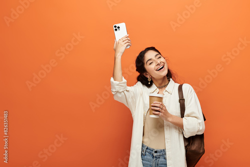 indian woman capturing moment with phone on vibrant orange backdrop.