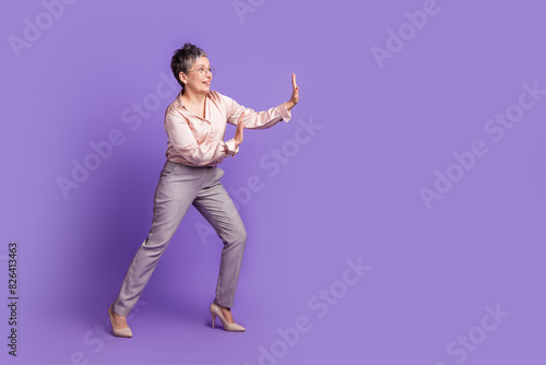 Full size photo of nice pensioner female push empty space wall wear trendy satin outfit isolated on violet color background