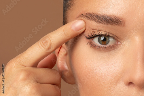 Closeup of young European woman pointing to the wrinkles on the upper eyelid, touching face. Blepharoplasty concept