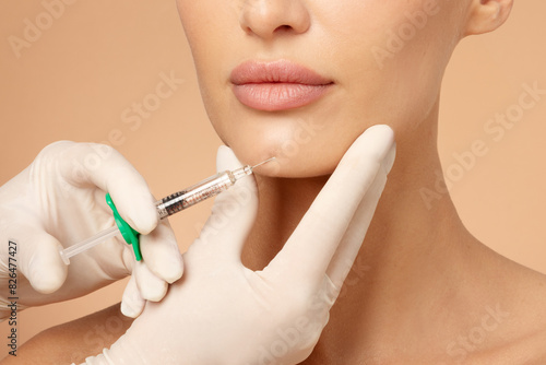 Cosmetologist holding syringe near woman's chin, beauty injections with fillers for chin shape correction, procedure chin contouring