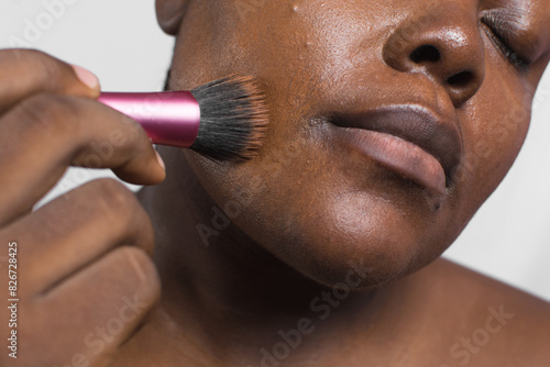Brown skinned woman applying foundation with makeup brush, dark skin woman using a stippling brush to apply foundation, process of applying foundation