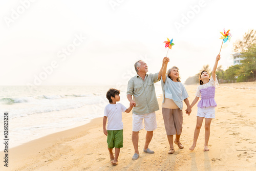 Happy Asian family travel ocean on summer holiday vacation. Grandparents and grandchildren boy and girl enjoy and fun outdoor lifestyle walking and playing together at tropical island beach at sunset.