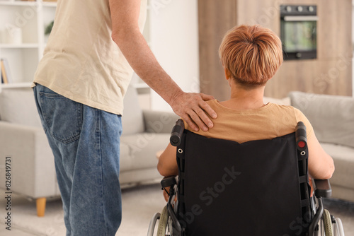 Mature woman in wheelchair with her husband at home, back view