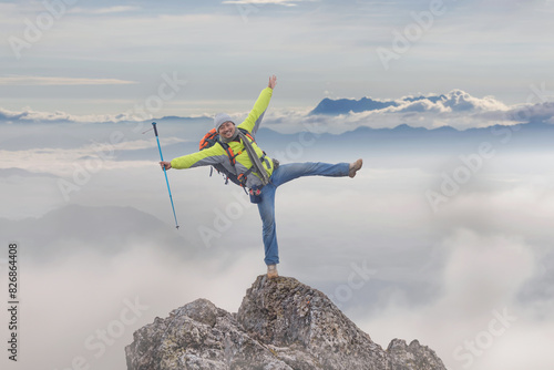 Hiker with backpack cheering elated and blissful with arms raised on top mountain foggy after hiking. Hiker men's hiking living healthy active
