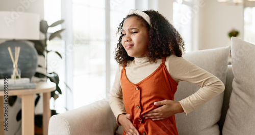 Young girl, stomach ache or allergies on couch in home for health problem or digestion recovery on weekend. Child, pain or food poisoning in living room with cramps for belly discomfort and suffering