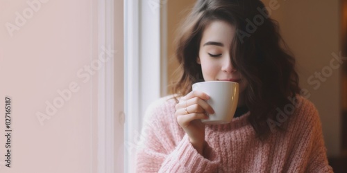 young woman enjoying a cup of freshly brewed hot tea at home. beautiful woman with cup of coffee sitting home in living room by the window. lazy day off concept