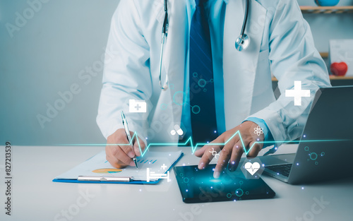 Male doctor using tablet to review treatment plan and write document reports in hospital office, Healthcare worker and doctor service, Digital laptop in modern office, Medical technology concept.