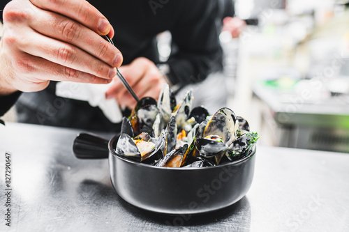 Close-up of chef hands mixing black mussels with a fork in a bowl, garnished with green herbs