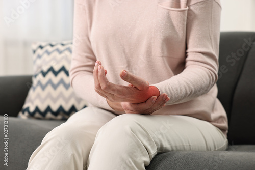 Woman suffering from pain in wrist on sofa, closeup