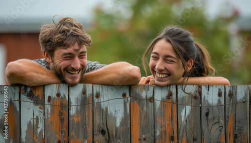 Neighbors leaning over a fence, both laughing as they share a humorous story, with copy space