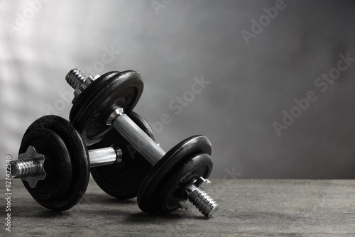 Two barbells on grey textured table, closeup. Space for text