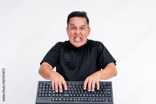 A middle aged man is angry and irate while typing furiously on his keyboard. Toxic online behavior or keyboard warrior concepts.