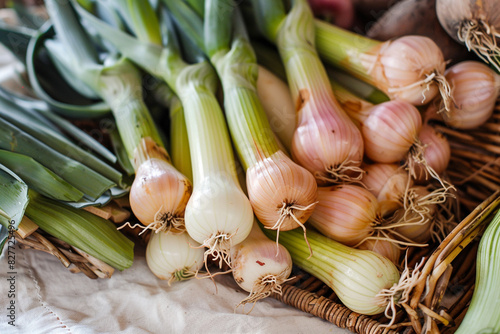 An assortment of fresh, organic shallots and leeks, their delicate flavors presented in a rustic wicker basket on a white canvas.