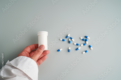 A hand holds a jar of white and blue pill on a blue background.
