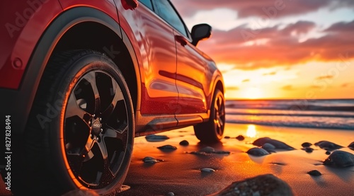  A red SUV was parked on the beach with a sunset background. 