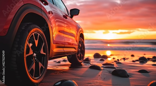  A red SUV was parked on the beach with a sunset background. 