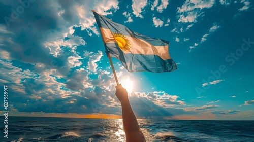 Argentina Independence Day. Hand with waving country flag against blue sky with clouds
