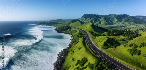 An aerial shot of a coastal highway with crashing waves on one side and lush green hills on the other, under a clear blue sky 32k, full ultra hd, high resolution