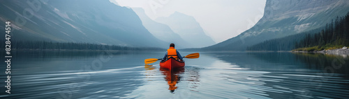 A man paddles a red canoe on a lake surrounded by mountains
