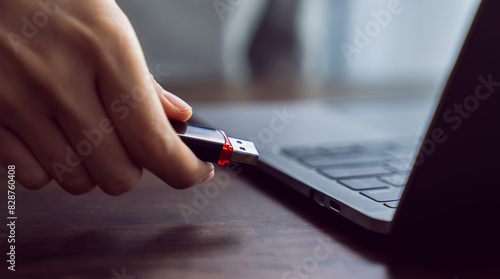 Hand holding usb flash drive with connecting to laptop at wooden table