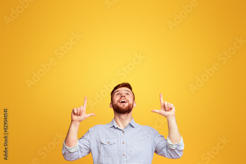 A man standing with hands in the air in front of a bright yellow background, pointing at copy space above him