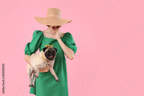 Surprised young woman with cute pug dog on pink background