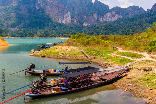 Wooden longtail boats on the shore of a lake surrounded by rainforest and cliffs (Khao Sok National Park)