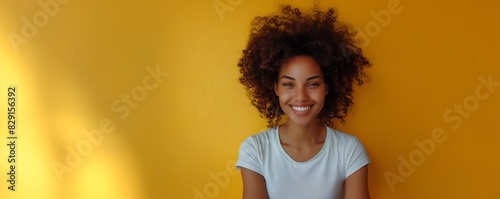 Mulher negra sorridente com cabelo volumoso estilho afro em um fundo solido amarelo