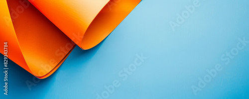 Orange paper, geometric shapes, and a flat lay design adorn a light blue background, exhibiting a minimalistic style.
