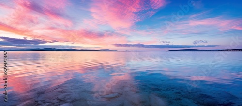 An idyllic seascape at sunset with clear blue skies vibrant pink clouds and gentle lighting The water reflects the symmetry of the surroundings acting as a natural mirror and showcasing the texture o
