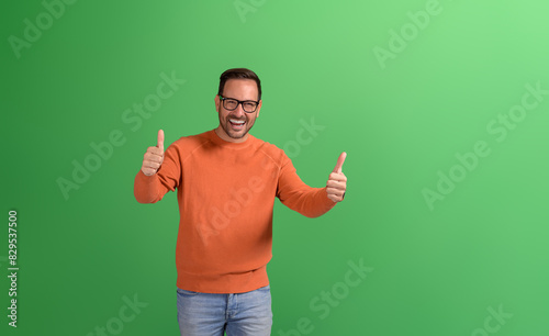 Portrait of successful male manager showing two thumbs up signs and laughing on green background