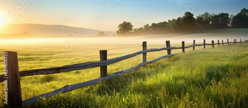 Morning light illuminates a rural farm fence with a copy space image of farmland and wild grass in the background