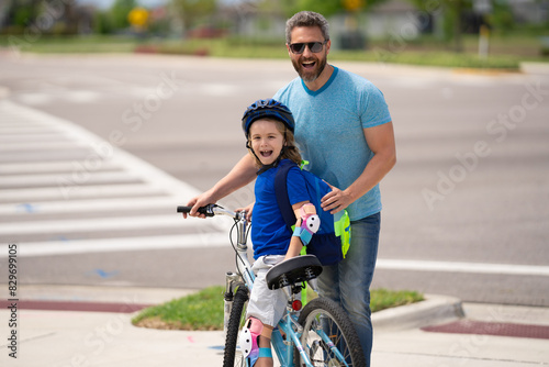 Father teaching son riding bike. Dad helping child son to ride a bicycle in american neighborhood. Child in bike helmet learning to ride cycle with father. Happy fathers day. Summer sport with child.