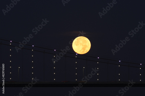 Full moon over Bosphorus bridge at night in Istanbul. The bright and full moon dominates the sky. Perfect for themes related to astronomy, lunar phases, and celestial events.