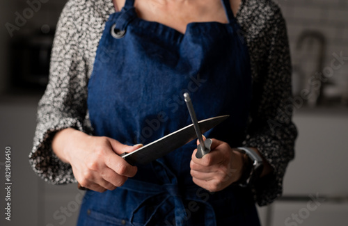 Woman Sharpens Knife In Kitchen Apron, Close-Up Of Hand In Focus