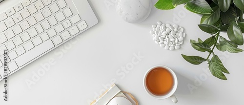 Clean workspace with keyboard, mouse, cup of tea, notepad, pills, and plant on white desk. Perfect for work and relaxation imagery.