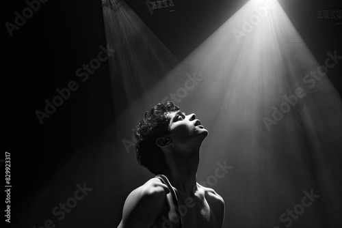 a man sitting on the ground in front of a light, An actor lost in the moment, embodying a thousand emotions on stage under a single spotlight
