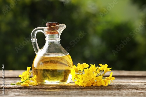 Rapeseed oil in glass jug and beautiful yellow flowers on wooden table outdoors