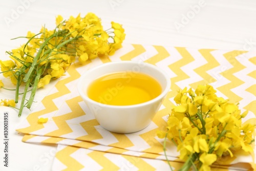 Rapeseed oil in bowl and beautiful yellow flowers on white table