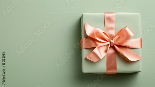 A beautifully wrapped gift box in pastel peach, featuring a decorative bow, positioned on a pastel green background using the golden ratio
