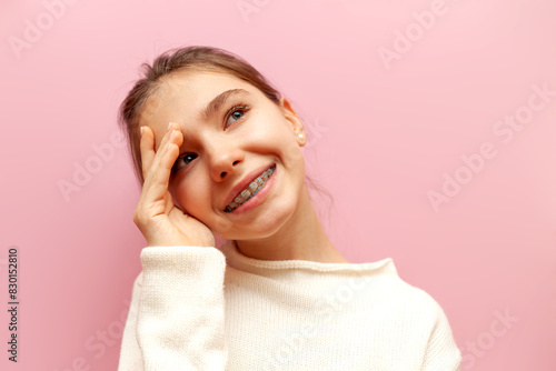 modest pensive teenage girl with braces thinks and imagines on a pink isolated background, the child is shy and plans and dreams