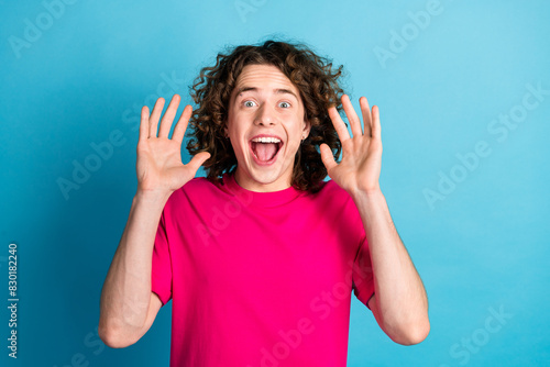 Portrait of eccentric man with curly hairstyle piercing wear pink shirt raising palm up open mouth isolated on blue color background