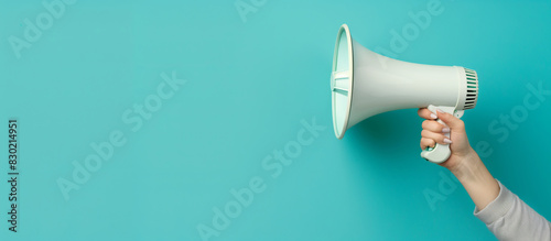 A woman's hand in a gray sweater holds a white loudspeaker on the right side on a blue background. Announces a discount promotion. Concept of recruitment, advertising. Banner. Copy space
