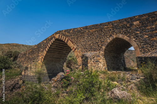 Ponte dei Saraceni. An ancient medieval bridge of Norman age located on the Simeto river. Adrano - Catania, in Sicily. Long exposure picture. June 2023