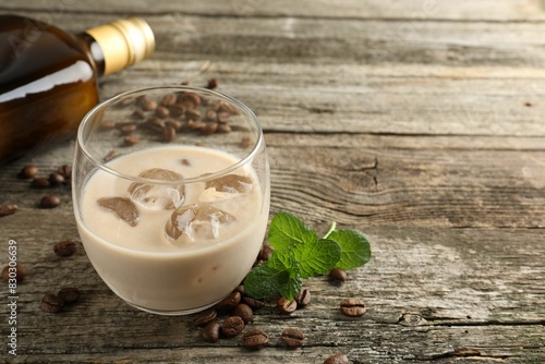 Coffee cream liqueur in glass, mint and beans on wooden table, space for text
