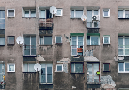 Poverty and misery of the Eastern Europe: old residential building of communist era. Facade wall with windows has plaster damage and includes satellite dish antenna and air conditioner.